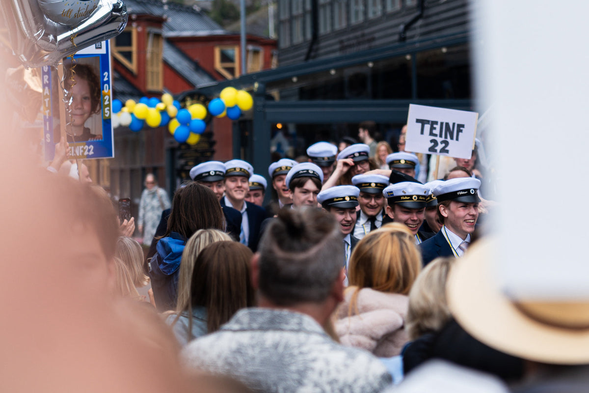 Studenter i vita studentmössor på studentdagen, omgivna av familj, ballonger och skyltar