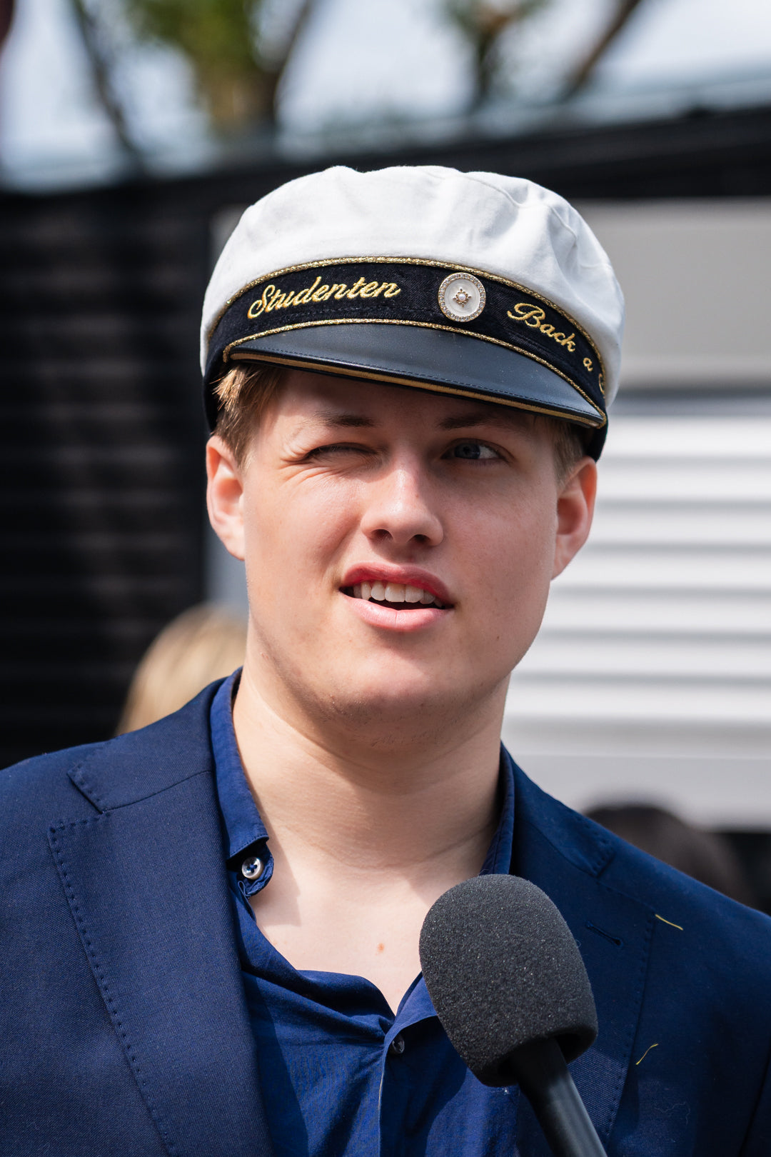 Student i studentmössa med ”Studenten” broderat på bandet intervjuas på studentdagen